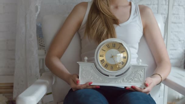 A young girl with art makeup sitting in a white armchair and holding a clock on her knees. — Stock Video