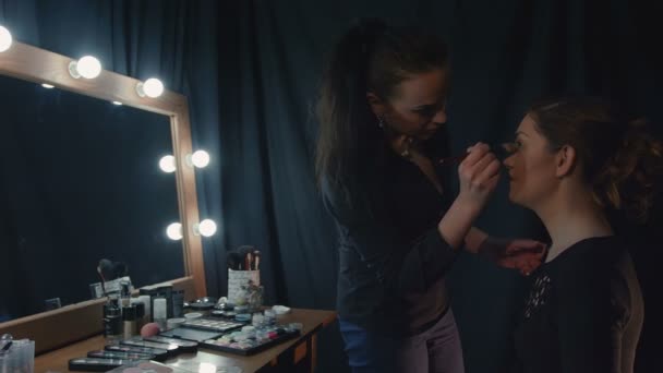 Женщина наносит макияж девушке возле зеркальных огней . — стоковое видео