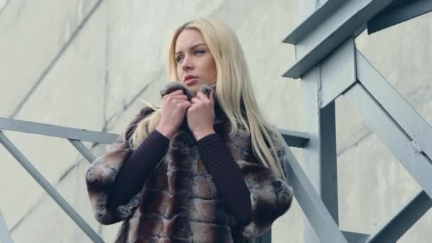 Módní venkovní video krásná smyslná dívka s blond vlasy, nosí luxusní kožich na pozadí kovových konstrukcí — Stock video