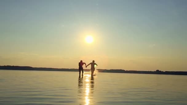 Zwei glückliche Homosexuelle, die bei Sonnenuntergang auf dem Wasser laufen — Stockvideo
