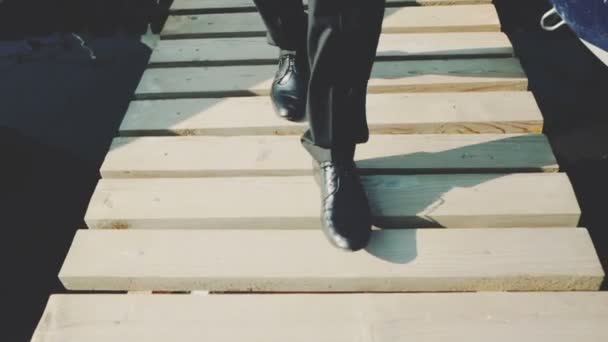Πόδια του ανθρώπου στα μαύρα παπούτσια περπάτημα σε μια ξύλινη γέφυρα πάνω από το νερό — Αρχείο Βίντεο