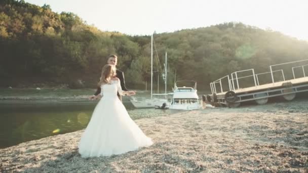 Casal de noiva e noivo bonito perto do iate do mar. Feliz casal recém-casado no casamento. Casal alegre casal de pé na praia . — Vídeo de Stock