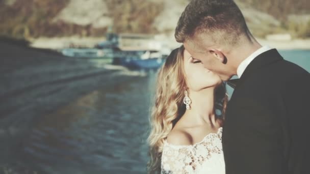 Hermosa novia rubia hermosa y elegante novio besándose en las rocas, en el fondo de un mar, ceremonia de boda en cyprus — Vídeo de stock