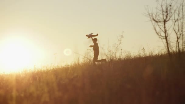 Мальчик с самолетом в руках бежит по холму на закате — стоковое видео