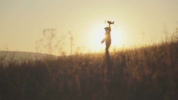 Jongen met het vliegtuig in hand draait op de achtergrond van de zonsondergang — Stockvideo