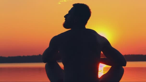 DOLLY MOTION: Bearded young athletic silhouette of a man sitting on the beach — Stock Video