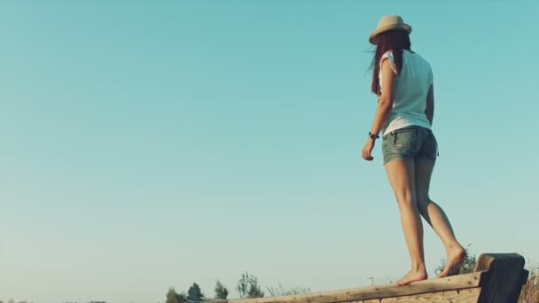 Mladá dívka v bílém klobouku je na okraji staré lodi na letní beach — Stock video