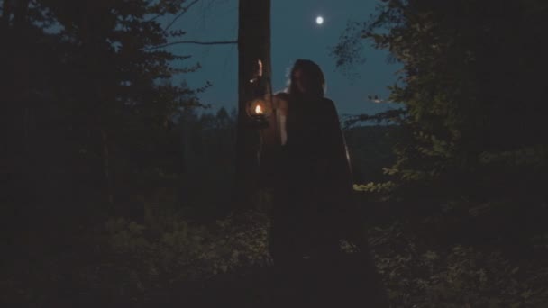 Natt. Kvinna i mystisk skog i en regnrock med en huva med en lykta går skog — Stockvideo