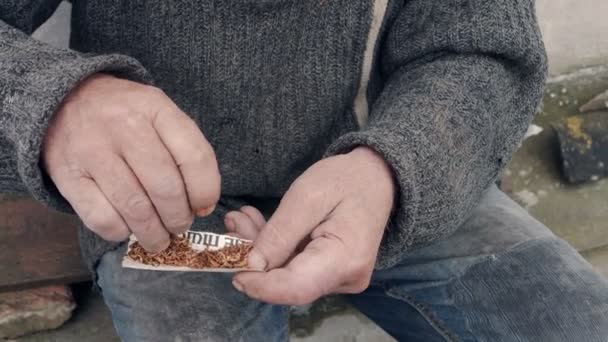 El pobre hombre desafortunado hace un cigarrillo con tabaco y un pedazo de papel — Vídeos de Stock