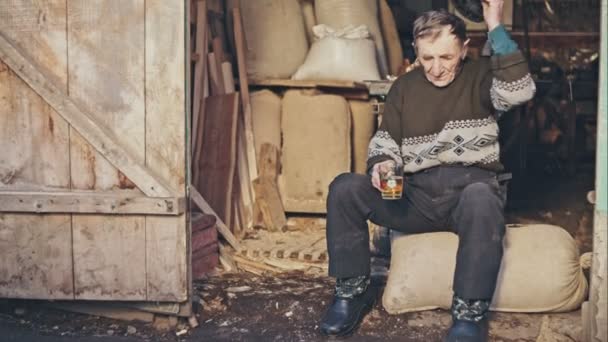 Atmosfera vecchio nonno in un cappello seduto su un sacco di farina intorno a bere birra fienili . — Video Stock