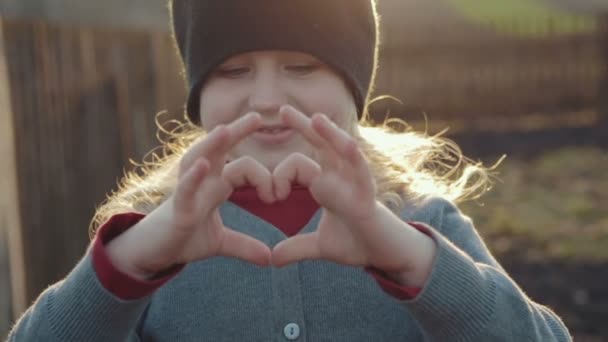 Maravillosa chica dobló sus manos en forma de corazón en un día soleado brillante . — Vídeos de Stock