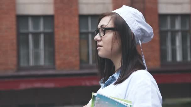 Portrait de l'école de médecine étudiante. La fille en lunettes et vêtements médicaux avec des manuels à la main souriant . — Video