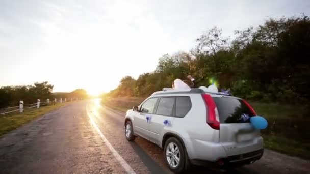 A newlywed couple is driving a car on road for their honeymoon — Stock Video