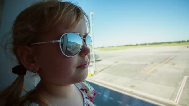 Liten flicka på flygplatsen ser ut genom fönstret. Glose upp. — Stockvideo