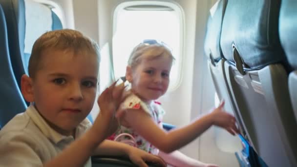 Boy with girl joyfully waving their hands while sitting in a chair airplane travel — Stock Video