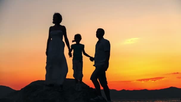 Silhouet van familie op het strand bij zonsondergang. Moeder toont de trend in de verte. De winderige. Ruwe videoverslag. — Stockvideo