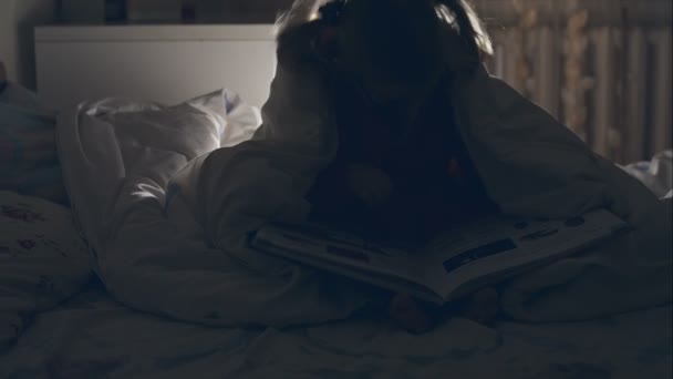 A young girl reading a book under the covers with a flashlight. RAW video record. — Stock Video