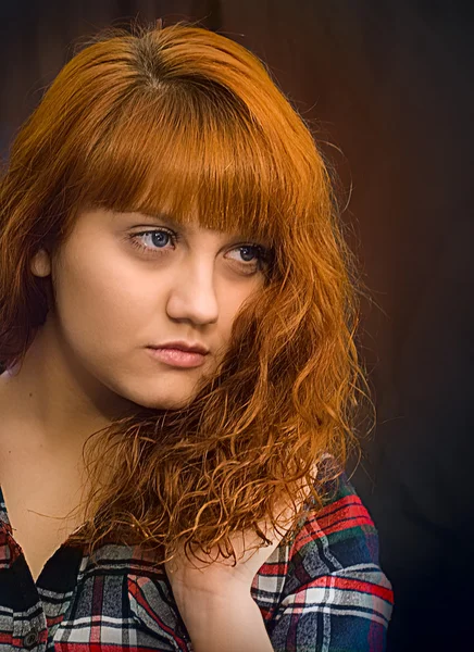 Young woman with orange hair in a red plaid shirt.  Portrait.
