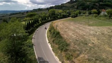 İtalya 'nın Toskana kentindeki dolambaçlı yolda motosiklet süren çiftlerin hava aracı videosu.