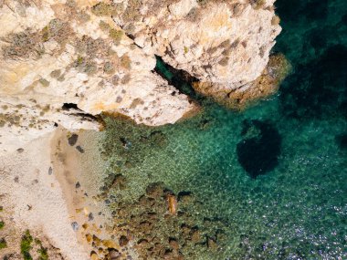 Açık turkuaz suların, batık karanlık bölgelerle kayalık kıyı şeridini karşılaması su altındaki araziyi ortaya çıkarıyor. Elba İtalya