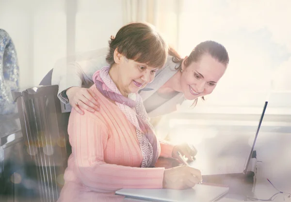 Mujer más joven ayudando a una persona mayor que utiliza el ordenador portátil para la búsqueda en Internet. Jóvenes y generaciones en edad de jubilación trabajando juntos . —  Fotos de Stock