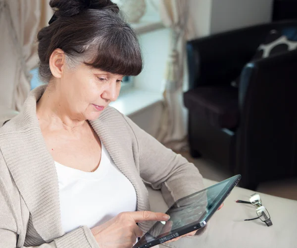 Edad de jubilación mujer de buen aspecto que mira a Internet en el dispositivo de la tableta. Vista desde arriba —  Fotos de Stock