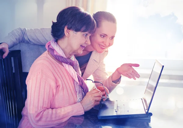 Fiatalabb nőt segít egy idős ember használ laptop számítógép internetes keresés. Fiatal és pension kor generációk együtt dolgoznak. — Stock Fotó