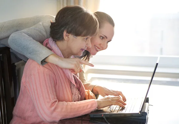 Fiatalabb nőt segít egy idős ember használ laptop számítógép internetes keresés. Fiatal és pension kor generációk együtt dolgoznak. — Stock Fotó