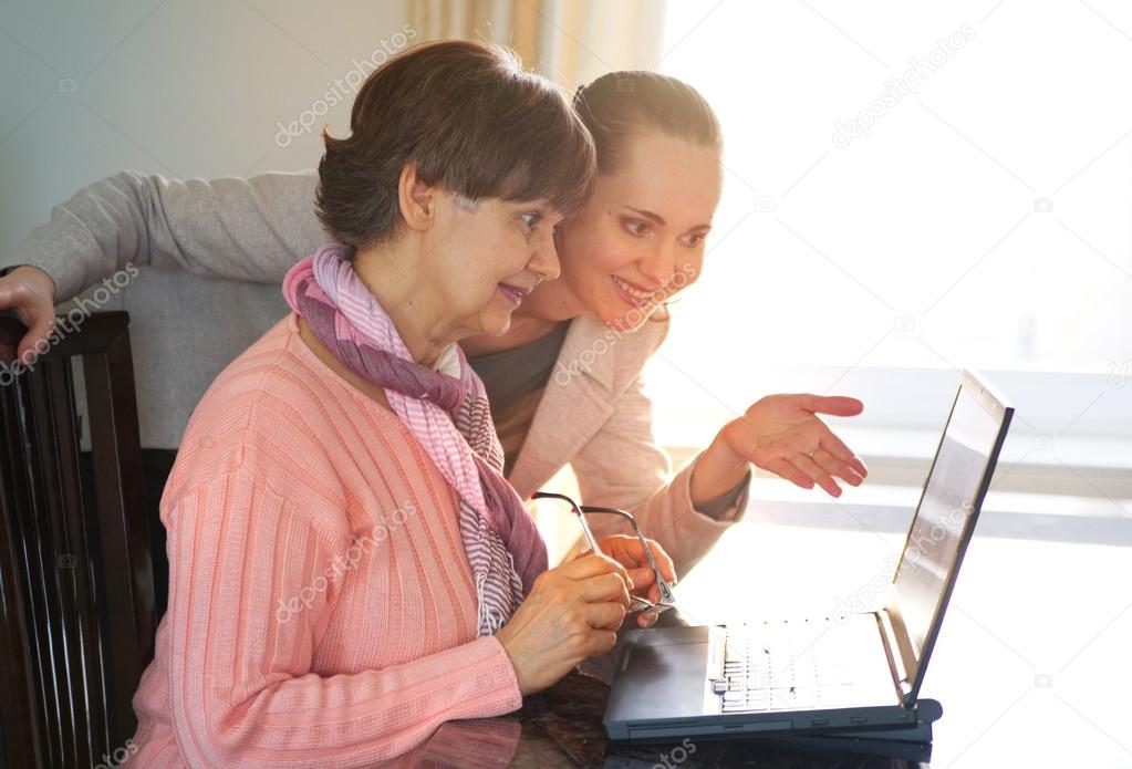 Younger woman helping an elderly person using laptop computer for internet search. Young and pension age generations working together.