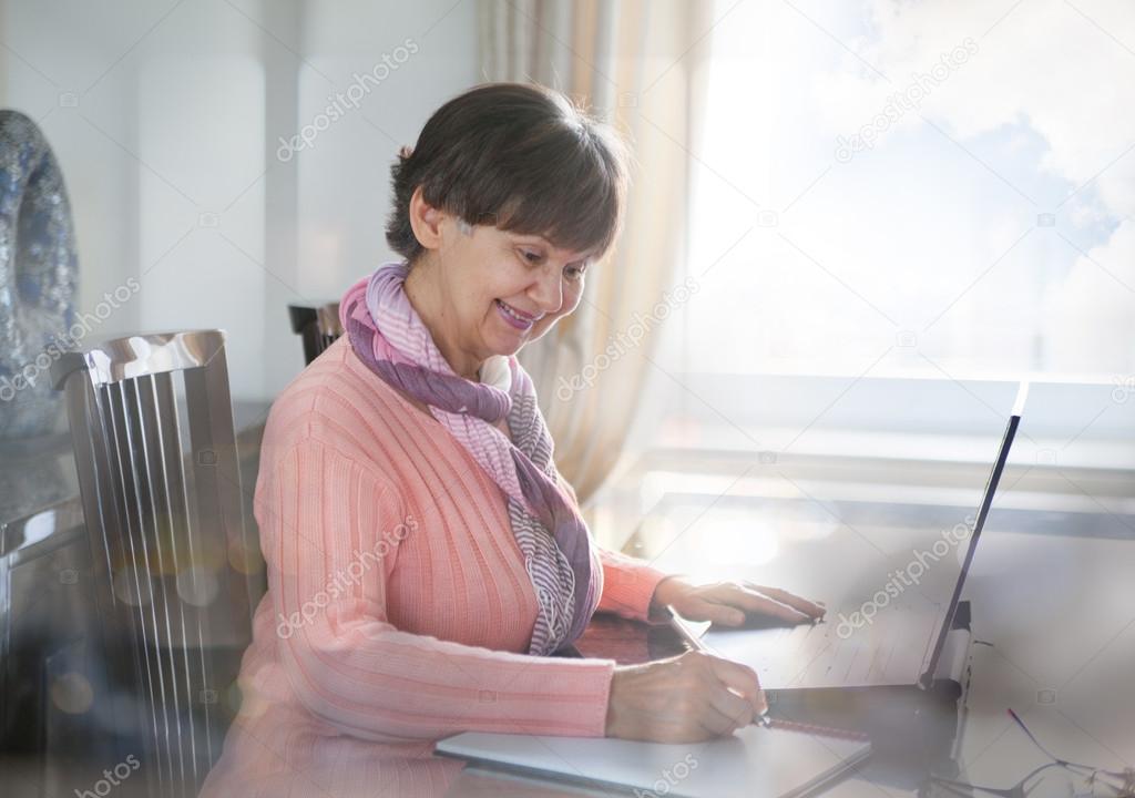 Elderly good looking woman working on laptop. Portrait in domestic interior