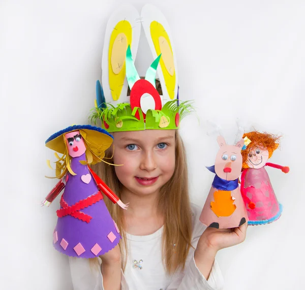 Little girl demonstrating her craft works Easter bonnet, paper dolls and reindeer — Stock Photo, Image