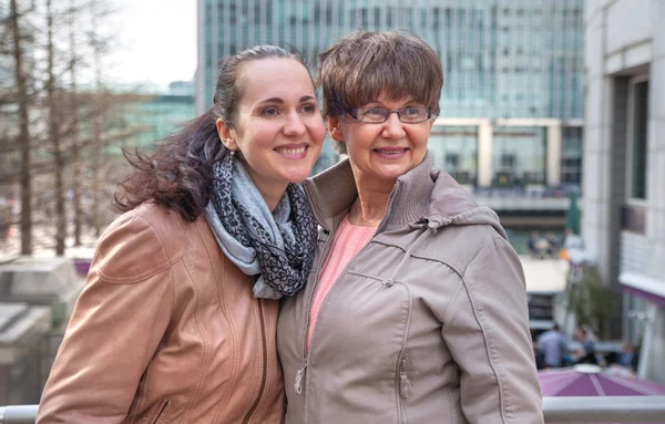 Outdoor family portrait of pension age Mother and her daughter in the city, smiling and looking around. Two generation, happiness and care  concept — Stock Photo, Image