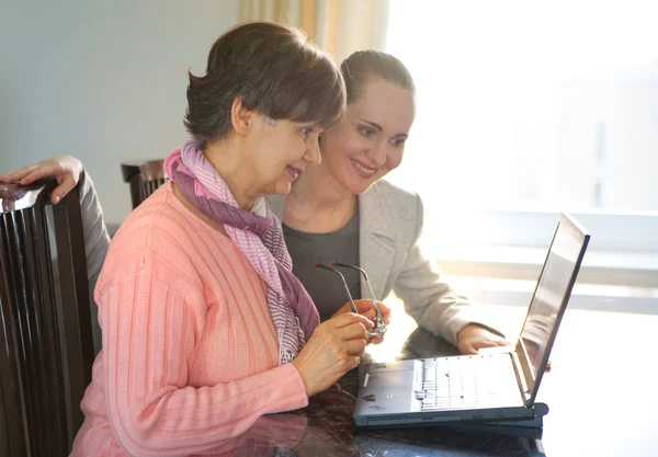 Genç kadın yaşlı bir kişi dizüstü bilgisayar Internet arama kullanarak yardım. Nesiller birlikte çalışan genç ve emeklilik yaş.