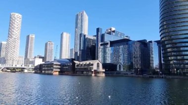 Londra, İngiltere - 7 Ekim 2025: Güneşli bir günde modern gökdelenler ve deniz kenarında yürüyen insanlarla Millwall rıhtımı manzarası. Köpekler adası, Canary Wharf.
