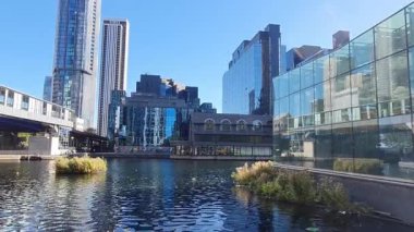 Londra, İngiltere - 7 Ekim 2025: Güneşli bir günde modern gökdelenler ve deniz kenarında yürüyen insanlarla Millwall rıhtımı manzarası. Köpekler adası, Canary Wharf.