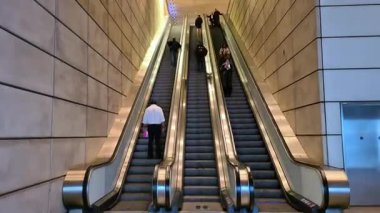 Londra, İngiltere - 31 Ekim 2025: Modern bir ulaşım istasyonunun lobisinde yürüyen merdivende hareket eden insanların zaman aşımı, şehir içi ulaşımı, hızlı şehir hayatı ve dinamik toplu taşıma altyapısını sembolize ediyor.