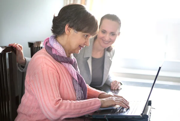 Yngre kvinna att hjälpa en äldre person med bärbar dator för sökning på internet. Unga och pension ålder generationer arbetar tillsammans. — Stockfoto