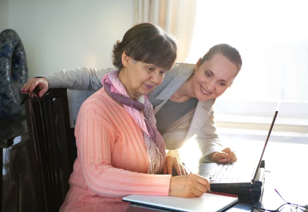 Yngre kvinna att hjälpa en äldre person med bärbar dator för sökning på internet. Unga och pension ålder generationer arbetar tillsammans. — Stockfoto