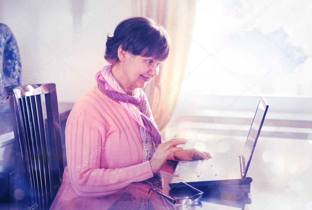 Elderly good looking woman working on laptop. Portrait in domestic interior