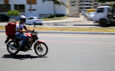 Salvador, Bahia, Brezilya - 6 Ocak 2021: Salvador 'da Pituba Mahallesi' nde uygulamalı olarak gıda teslimatçısı motosiklet sürerken görüldü..