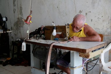 Salvador, Bahia, Brezilya - 8 Şubat 2021: Salvador şehrindeki Barroquinha bölgesinde bir zanaatkar deri atölyesinde bir makine ile dikiş dikiyor..