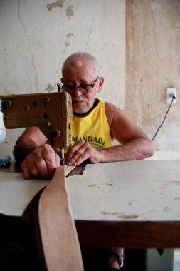 Salvador, Bahia, Brezilya - 8 Şubat 2021: Salvador şehrindeki Barroquinha bölgesinde bir zanaatkar deri atölyesinde bir makine ile dikiş dikiyor..