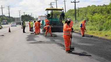 Camacari, Bahia, Brezilya - 24 Ağustos 2021: işçiler, Camacari şehrinin sanayi merkezine giriş yolunun asfalt özetini yaparken görülüyor..