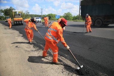 Camacari, Bahia, Brezilya - 24 Ağustos 2021: işçiler, Camacari şehrinin sanayi merkezine giriş yolunun asfalt özetini yaparken görülüyor..