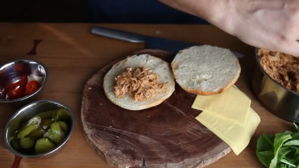 Chef haciendo un sándwich de cerdo tirado en un rollo fresco carga carne, queso, encurtidos, jalapeños y rúcula — Vídeos de Stock