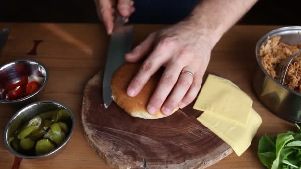 Chef haciendo un sándwich de cerdo tirado en un rollo fresco. Corta un bollo para cargar carne, queso, encurtidos, jalapeños y rúcula — Vídeos de Stock