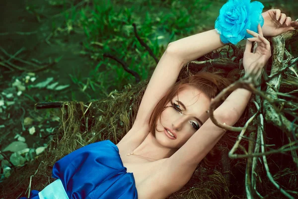 The girl in a blue dress lies on branches — Stock Photo, Image