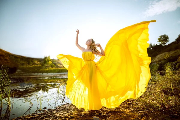A menina bonita com o cabelo longo no vestido fluttering amarelo Imagem De Stock