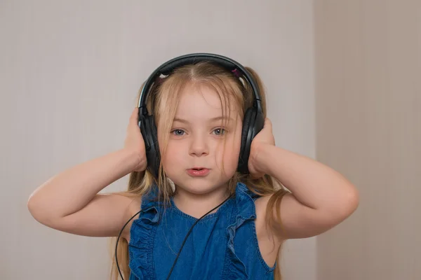 A menina bonita com um cabelo claro longo canta, mantém as mãos em grandes fones de ouvido pretos Imagens Royalty-Free