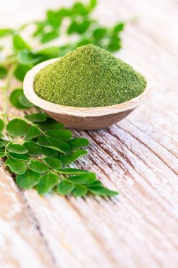 Moringa tozu (Moringa Oleifera) hindistan cevizi kasesinde, ahşap arka planda orijinal taze Moringa yapraklarıyla. Sağlıklı ürün, süper yiyecek, vitamin.